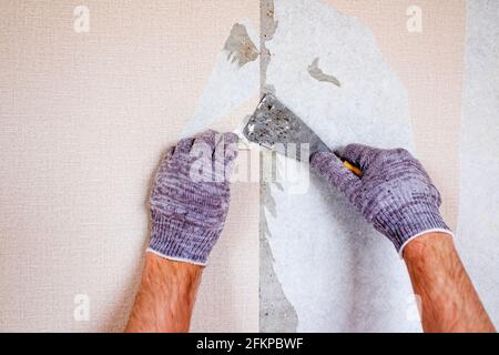 Processus de rénovation de l'appartement. Les mains de sexe masculin caucasien déchirent le vieux papier peint du mur se préparant à la décoration de la maison Banque D'Images
