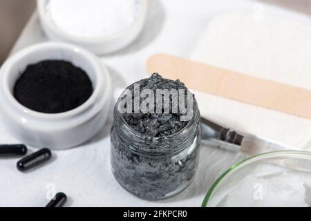 Ingrédients pour un masque facial au charbon de bois maison. Poudre de charbon de bois, huile de coco, argile cosmétique blanche. Concept beauté maison. Banque D'Images