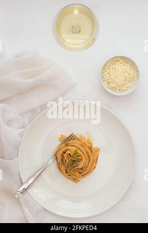 Plaque blanche pleine de spaghetti. Verre de vin blanc, petit bol rempli de parmesan. Arrière-plan blanc Banque D'Images