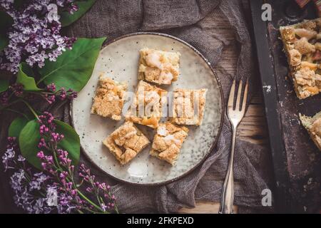 Morceaux de gâteau crumble à la rhubarbe sur une assiette sur un fond en bois, décoré de fleurs de lilas, vue du dessus Banque D'Images
