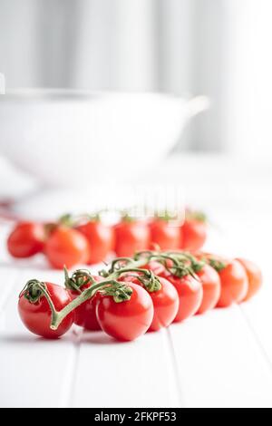 Tomates cerises rouges fraîches. Petites tomates sur branche sur table blanche. Banque D'Images