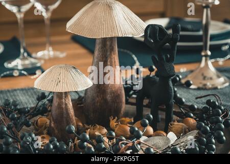 Gros plan de la décoration de table automnale avec champignons en bois, couronne de baies, noisettes et cerf en bois, dominés par le bleu foncé, l'argent et les couleurs du bois Banque D'Images