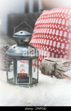 Lanterne argentée et un oreiller de Noël rouge et blanc sur une peau de mouton blanche sur une véranda en bois, photo de stock verticale. Banque D'Images