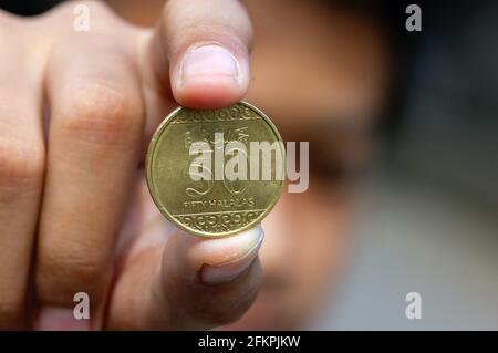 Main d'enfant asiatique tenant une cinquante pièces de monnaie à Riyal halalas, l'argent de l'Arabie Saoudite, foyer choisi Banque D'Images