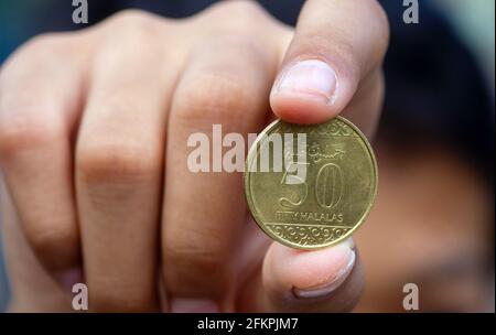 Main d'enfant asiatique tenant une cinquante pièces de monnaie à Riyal halalas, l'argent de l'Arabie Saoudite, foyer choisi Banque D'Images