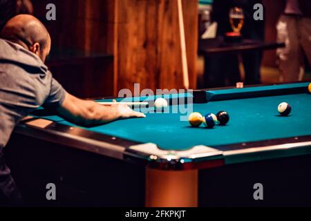 Un homme jouant au snooker, se tordu pour frapper le ballon blanc sur la table de billard de la piscine. Banque D'Images