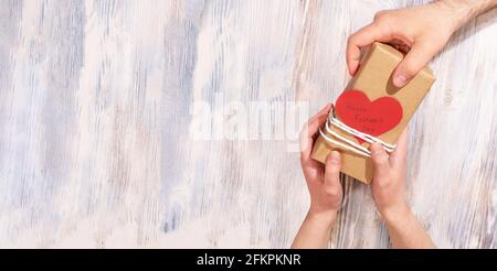 Mains d'une adolescente donnant le cadeau de fête du père avec une carte en forme de coeur à papa sur un fond blanc en bois, bannière, gros plan. Banque D'Images