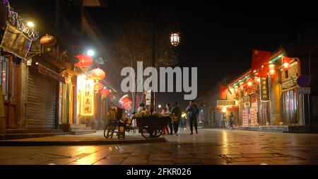 Pingyao dans la province du Shanxi, Chine : scène de rue à Pingyao la nuit avec lumières de la ville, lanternes rouges et drapeaux chinois. Les gens qui marchent dans la vieille ville. Banque D'Images