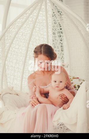 Jeune mère tenant son nouveau-né. Maman allaitant bébé. Femme et nouveau-né dans la chambre blanche. Mère jouant avec un enfant en train de rire. La famille à la maison Banque D'Images