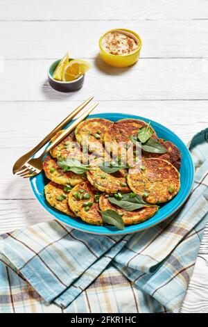 crêpes d'épinards aux pois chiches sur une assiette bleue sur une table en bois blanc avec houmous dans un petit bol, vue verticale Banque D'Images