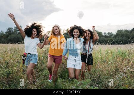 Quatre femmes riant appréciant des vacances d'été. Des amis heureux qui s'exécutent sur le terrain. Banque D'Images
