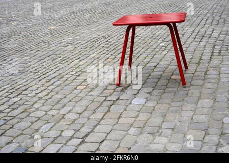 Tabouret en métal rouge placé sur une chaussée en pierre de pierre à galets dans le centre historique de Berne en Suisse. Il y a beaucoup d'espace de copie. Banque D'Images