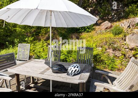 Vue sur deux casques pour les sports actifs, posés sur une table en bois avec chaises et parasol. Suède. Europe. Banque D'Images