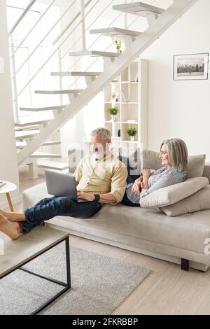 Un couple d'âge mûr heureux utilisant des appareils se détendant à la maison sur un canapé. Banque D'Images