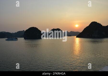 Vue panoramique du coucher de soleil sur les eaux étincelantes, les formations rocheuses, les montagnes bleues et les bateaux flottants sur la baie de Halong au Vietnam Banque D'Images