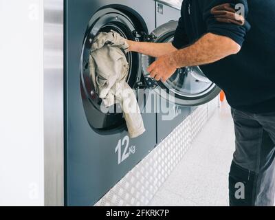 Les mains pour charger le linge dans le lave-linge au niveau des nettoyeurs à sec. Concept de nettoyage Banque D'Images