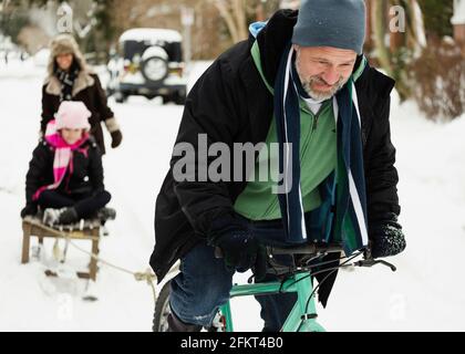 Les parents et la fille jouant avec toboggan dans la neige Banque D'Images