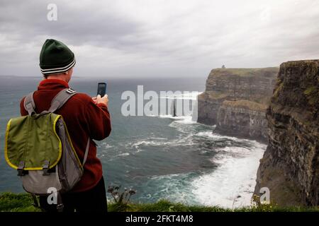 Mid adult man taking photo, les Falaises de Moher, le Burren, comté de Clare, Irlande Banque D'Images