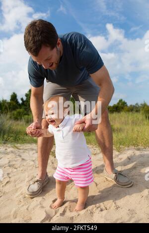 Mid adult man holding baby filles mains tandis que d'une façon incertaine dans le sable Banque D'Images