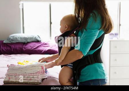 Mid adult woman travaux domestiques avec sa petite fille à porte-bébé Banque D'Images