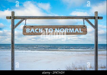 Panneau en bois avec texte de retour à la normale contre le ciel bleu, la mer et la plage avec le sable blanc. Concept de voyage et de vacances. Banque D'Images