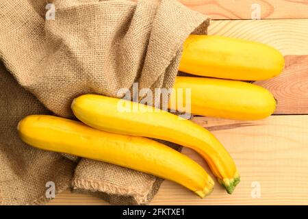 Quatre courgettes juteuses mûres, jaunes avec un sac de jute, gros plan, sur une table en bois, vue de dessus. Banque D'Images