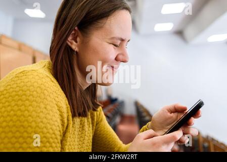 Femme en chandail jaune souriant et utilisant un smartphone, portrait de gros plan. Banque D'Images