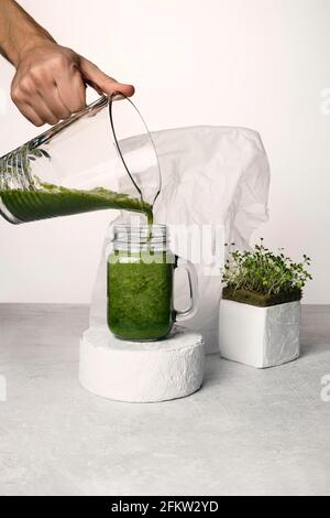 Cocktail Microgreen sur podiums en béton. Une main d'homme verse un cocktail de micro-vert dans un verre. Sur un fond blanc et concret. Banque D'Images