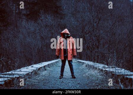 Homme dans une veste à capuchon orange avec le masque à gaz face à l'ancien viaduc de chemin de fer en pierre abandonné Banque D'Images