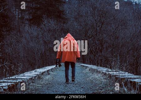 Homme en veste à capuchon orange avec le masque en main sur le viaduc de chemin de fer en pierre abandonné. Banque D'Images