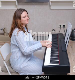 Une femme adulte dans une chemise de nuit bleue joue de la musique un piano à la maison Banque D'Images