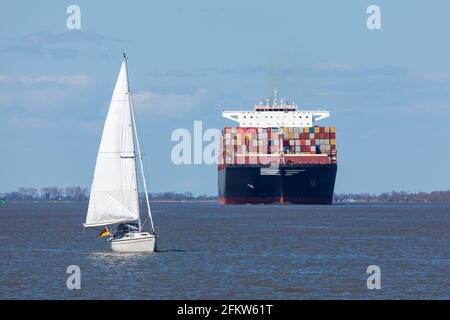 Petite croisière en bateau à voile devant un énorme bateau à conteneurs sur la rivière Elbe. Concentrez-vous sur le voilier. Banque D'Images