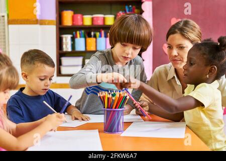 Éducateur et groupe d'enfants dans la peinture internationale de maternelle avec crayons de cire Banque D'Images