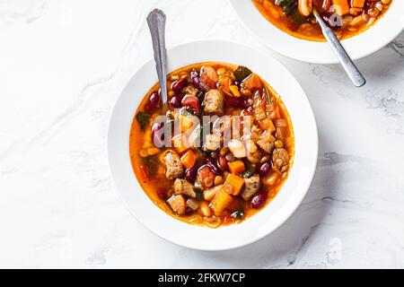 Soupe de haricots avec saucisses dans une assiette blanche, fond en marbre blanc. Concept de cuisine italienne. Banque D'Images