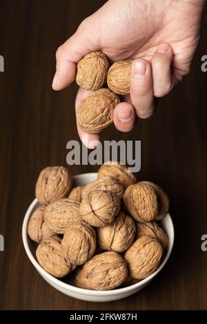 Main de l'homme ramassant trois noix dans un bol Banque D'Images