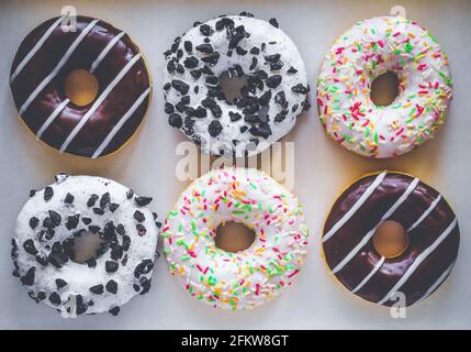 Flat Lay image de six beignets en anneau avec glaçure blanche et des centaines et milliers de couleurs, chocolat et rayures et glaçure blanche avec biscuits noirs Banque D'Images