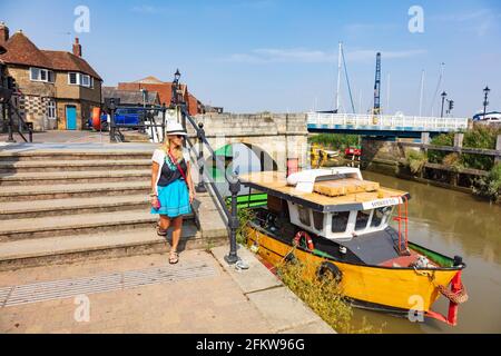 Belle femme en robe turquoise, marche à pied du pont à péage Sandwich sur quai, Kent, Royaume-Uni Banque D'Images