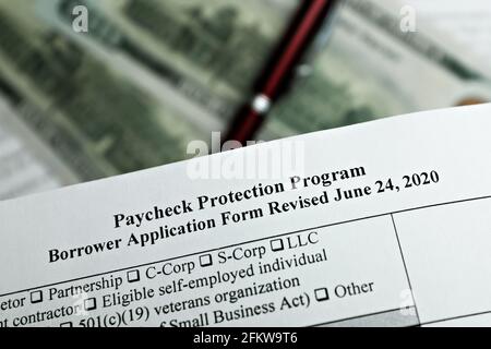 photo sélective du formulaire de demande d'emprunteur du programme de protection des chèques de paie révisé, sur fond de billets en dollars et d'un stylo Banque D'Images