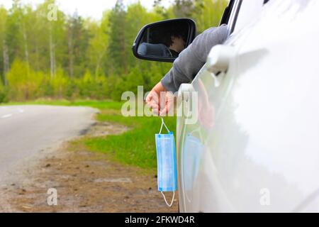 Le conducteur d'un SUV blanc lance un masque médical usagé par la fenêtre. La fin de la pandémie du coronavirus. Le concept de voyager en voiture. Retour à NOR Banque D'Images