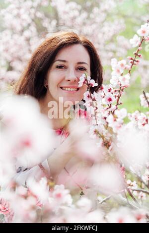 Belle femme brune dans une robe avec des fleurs marche à travers le jardin fleuri au printemps Banque D'Images