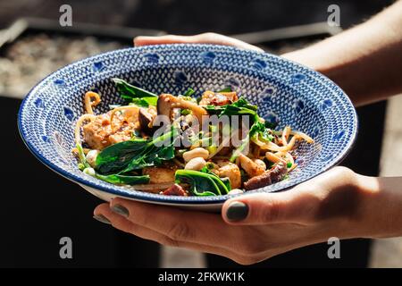 Mains tenant le tofu frite avec des épinards et des noix Banque D'Images