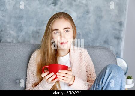 Jeune belle femme portant un t-shirt blanc sur un canapé en tissu gris à la maison. Jolie femme mince dans une situation domestique, reposant sur un canapé dans son haut Banque D'Images