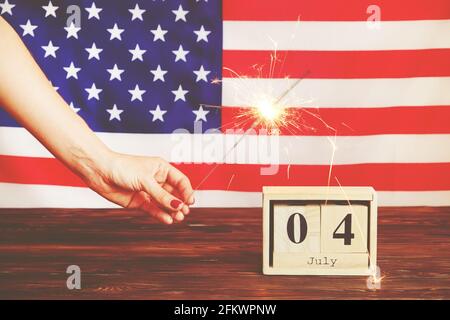 Photo courte aux tons rétro, femme tenant un sparkler brûlant, lumière bengale sur fond de drapeau américain. 4 juillet, USA jour de l'indépendance date sur bois c Banque D'Images