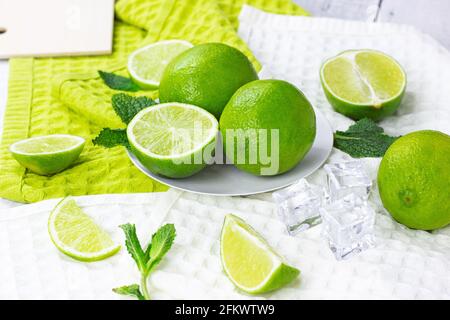 Des limes et des tranches de citron vert frais juteux avec des feuilles de menthe dans la cuisine sur fond clair. Banque D'Images