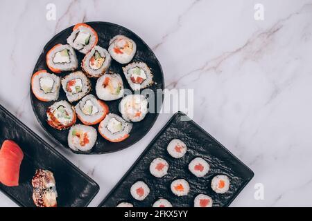 Menu du bar à sushis pour le déjeuner - différents petits pains à sushis avec saumon, avocat et anguille smockée sur fond de table en marbre blanc avec espace pour les copies - futomaki. Uramaki Banque D'Images