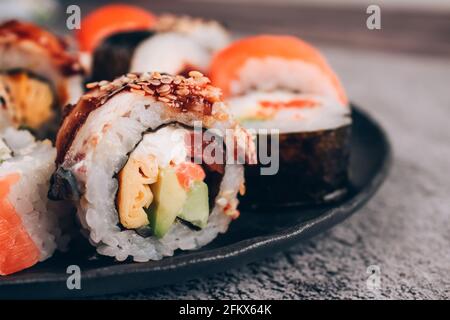 Menu du bar à sushis pour le déjeuner. Vue rapprochée des petits pains à sushi avec saumon, avocat et anguille en béton sur le fond de la table - futomaki. Uramaki, hosomaki Banque D'Images