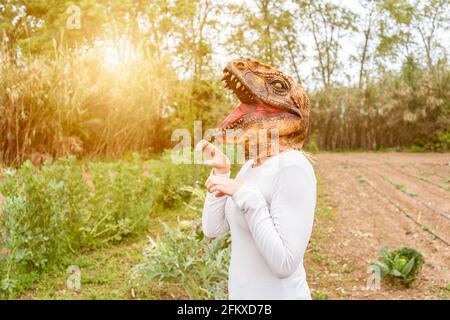 Femme avec masque de tête de dinosaure dans le jardin de légumes au coucher du soleil.Copy espace Banque D'Images