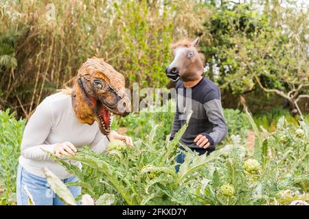 Couple heureux homme et femme avec dinosaure et masque de tête de cheval dans le jardin de légumes. Fantaisie et humour style de vie concept. Banque D'Images