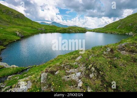 paysage avec lac dans les montagnes. magnifique paysage d'été nature sur une journée nuageux. destination de voyage populaire de fagaras crête, roumanie. herbe et sto Banque D'Images