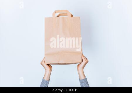Mains de femme tenant le fond du sac de papier kraft brun avec poignées sur fond blanc Banque D'Images